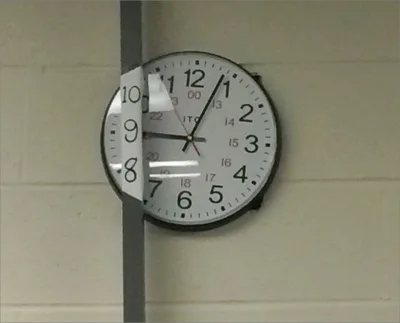 Photo of a wall clock partly hidden behind a vertical pillar. The numbers 10, 9, and 8 are blocked by the pillar, so someone has drawn those missing numbers directly on the pillar to make the clock readable again.